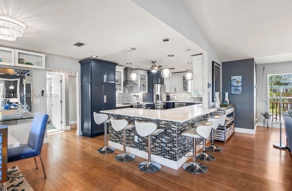 Kitchen featuring custom navy and white cabinetry, stone-finish countertops, multi-tonal mosaic tile breakfast bar, pendant lighting, and wood-finish 