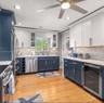 Kitchen featuring two-tone custom cabinetry, stone mosaic backsplash, quartz countertops, stainless steel appliances, and wood-finish flooring