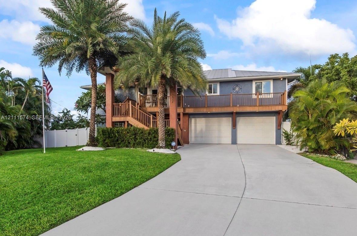 Two-story residence featuring a concrete driveway, two-car garage, expansive second-level deck with wooden railings, and mature palm trees
