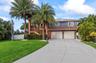 Two-story residence featuring a concrete driveway, two-car garage, expansive second-level deck with wooden railings, and mature palm trees