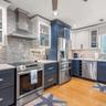 Kitchen featuring two-tone cabinetry, stainless steel appliances, a glass-tile backsplash with decorative accent, solid surface countertops, and wood-