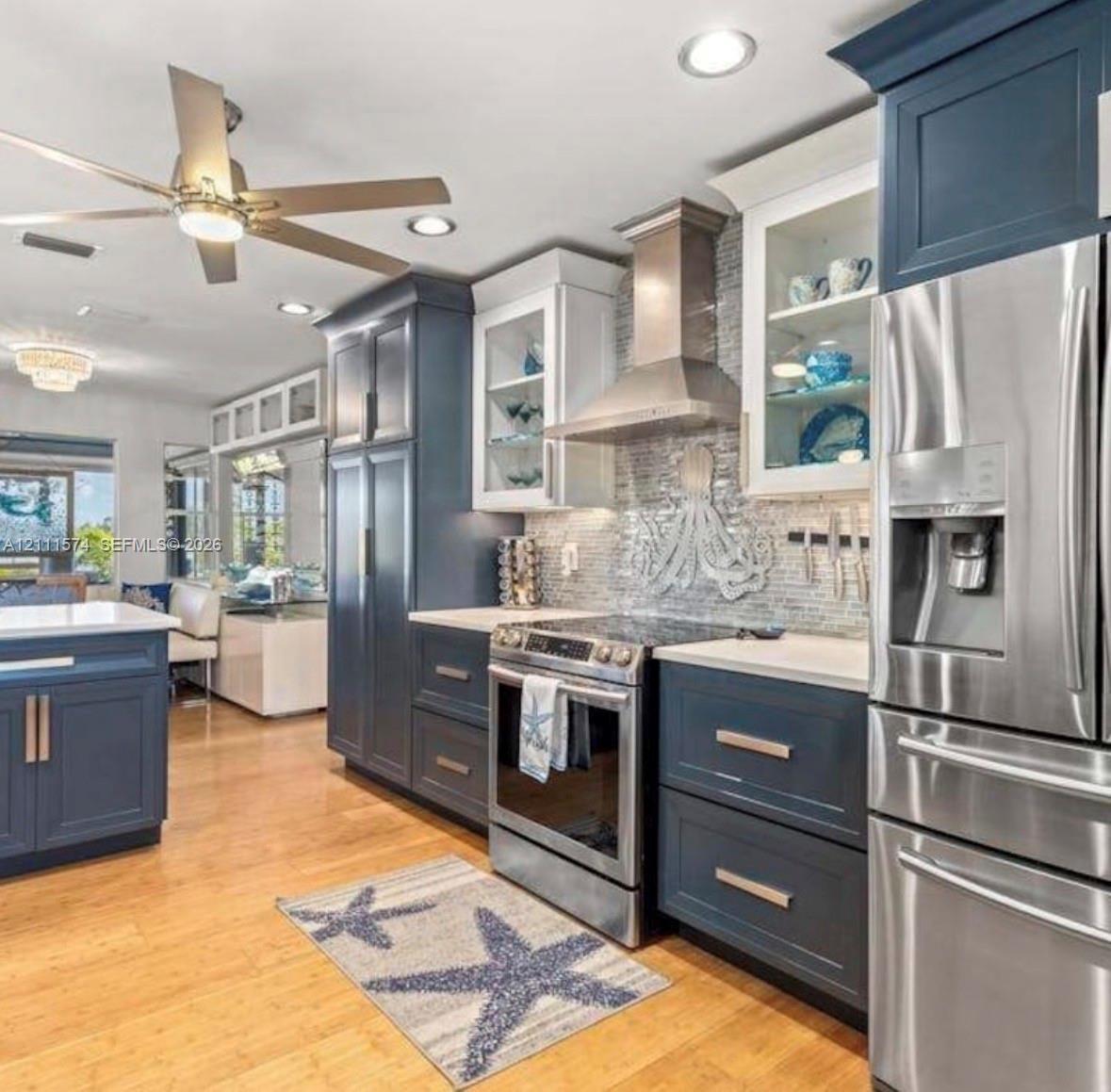 Kitchen featuring dual-toned navy and white cabinetry, stone-finish countertops, stainless steel appliances, a tile backsplash, and wood-finish floori