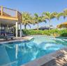 In-ground swimming pool with tile border, elevated wood-finish deck, stone paver pool deck, and mature palm trees