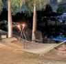 Waterfront backyard featuring mature palm trees and a circular stone fire pit
