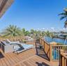 Elevated wooden deck featuring a perimeter railing, overlooking a canal and a swimming pool with mature palm trees