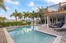 In-ground swimming pool with a stone paver deck, elevated wood-tone balcony, and covered lower-level patio area