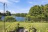 Backyard featuring a manicured lawn, established shrubbery, a black metal chain-link fence, and direct water frontage with dense natural perimeter tre