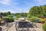 Paver patio featuring a decorative stone-tiled fire pit and perimeter landscaping with mature trees overlooking a waterfront backdrop