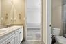 Bathroom featuring a dual-sink vanity with white cabinetry, stone-finish countertops, tile backsplash, and large wall-mounted mirror