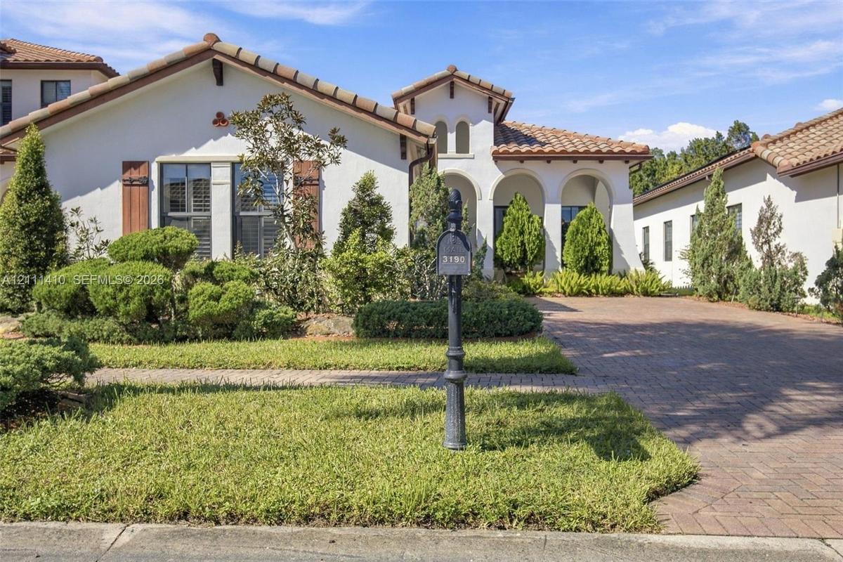 Stucco exterior featuring arched entryways, a terracotta-style tile roof, decorative wood shutters, and a paved brick driveway