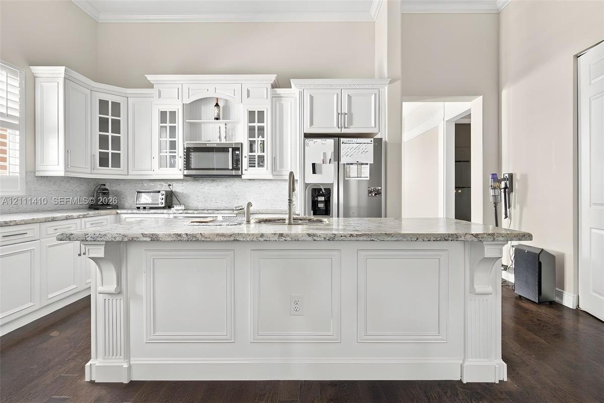 Kitchen featuring white cabinetry with crown molding, stone countertops, a large center island with corbel detailing, stainless steel appliances, and 