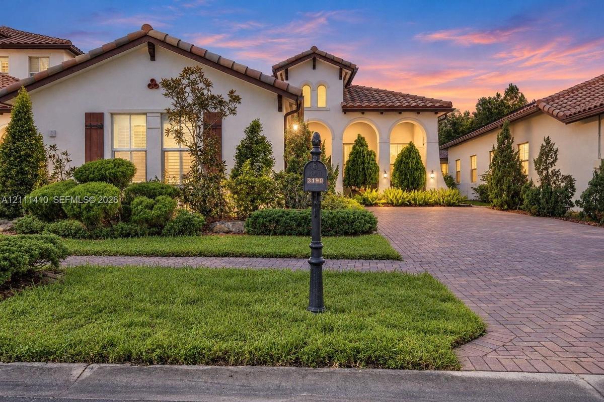 Stucco exterior featuring arched entryways, a terracotta-style tile roof, wood shutter accents, and a paver driveway