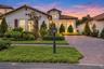 Stucco exterior featuring arched entryways, a terracotta-style tile roof, wood shutter accents, and a paver driveway
