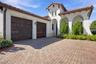 Stucco exterior featuring arched entryways, a terracotta-style tile roof, dual wood-finish garage doors, and a herringbone-patterned paver driveway