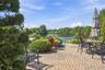 Paver patio featuring integrated string lighting, mature landscaping, and waterfront access