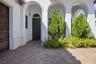 Covered entryway featuring arched architectural detailing, herringbone-patterned brick pavers, a solid wood-finish entry door with metal hardware, and