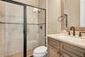 Shower with glass enclosure and black frame, vanity featuring a stone countertop and rectangular undermount sink, dark-finished hardware, and tile wal
