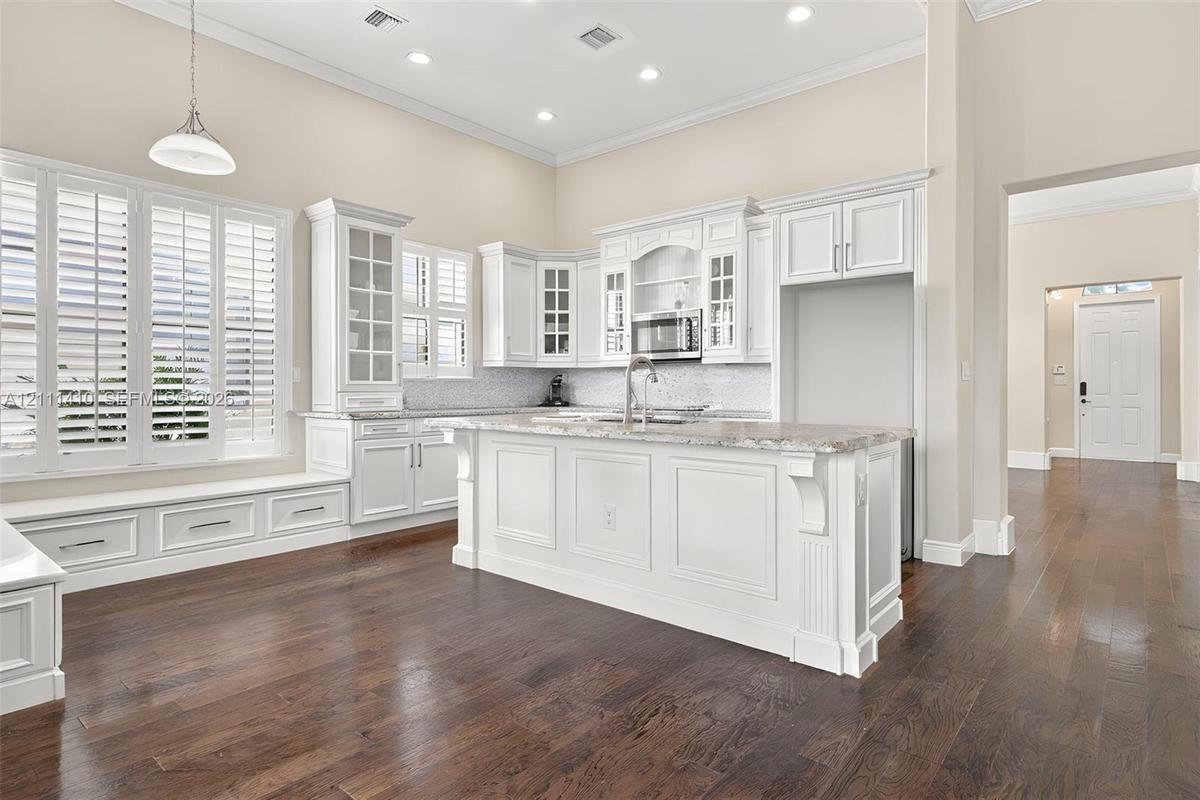 Kitchen featuring white cabinetry with glass-front uppers, a central island with stone-finish countertops, recessed lighting, plantation shutters, and