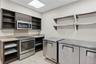 Kitchen area featuring dark wood-finish cabinetry, stainless steel appliances, open shelving, stone-composite countertops, and tile flooring