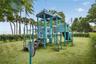 Outdoor recreational structure featuring dual-level platforms, multiple slides, integrated climbing apparatuses, and synthetic turf ground cover