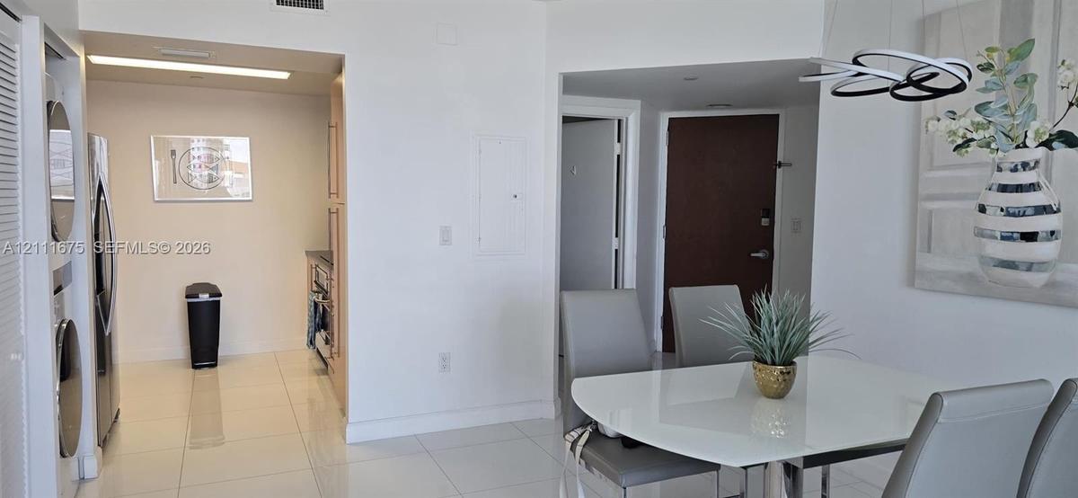 Large-format white tile flooring, stacked laundry appliance enclosure, and contemporary architectural lighting fixture