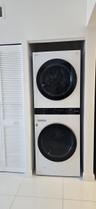 Stacked laundry unit featuring a white finish with front-loading glass-panel doors, complemented by white louvered closet doors and large-format tile 