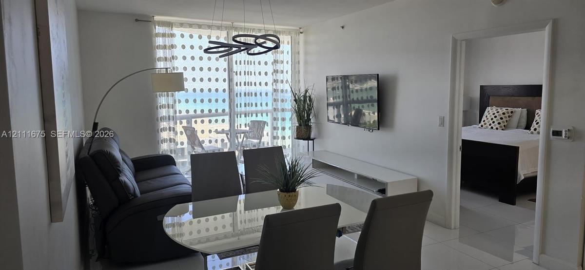 Living area featuring tile flooring, floor-to-ceiling glass sliding doors, modern circular pendant lighting, and an expansive balcony