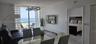Floor-to-ceiling glass balcony doors, sculptural overhead lighting fixture, white tile flooring, and coastal scenery