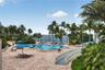 Outdoor swimming pool and spa surrounded by stone-paver decking, mature palm trees, and water frontage