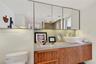Floating vanity featuring wood-finish cabinetry, a stone-surface countertop, white vessel sink, and an expansive wall-to-wall mirrored medicine cabine