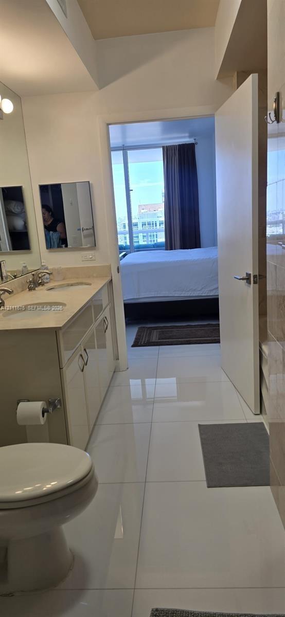 Bathroom featuring a dual-sink vanity with light-toned countertop, large wall-mounted mirror, and polished tile flooring