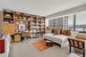 Built-in wall-to-wall wood shelving unit with integrated desk workspace and large windows featuring horizontal blinds
