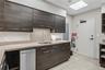 Kitchen area featuring dark wood-finish cabinetry, solid surface countertops, stainless steel undermount sink with gooseneck faucet, and tile flooring