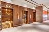 Elevator lobby featuring metallic geometric door panels, slatted wood wall cladding, exposed brick masonry pillar, recessed lighting, and tile floorin