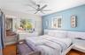 Bedroom featuring wood-finish flooring, a contemporary six-blade ceiling fan with integrated lighting, and a built-in white panel headboard with glass