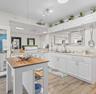 Kitchen featuring white shaker-style cabinetry, stone-finish countertops, wood-finish flooring, a stainless steel undermount sink, and a center island
