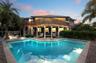 Multi-level elevated home featuring a wrap-around wooden deck, a ground-level covered patio area with support columns, and an inground swimming pool w