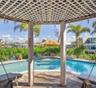 Covered gazebo featuring a lattice roof, stone paver flooring, and suspended bench seating, positioned over a swimming pool with water access