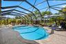 Screen-enclosed pool area featuring an in-ground pool, elevated spa, and stone-paver decking