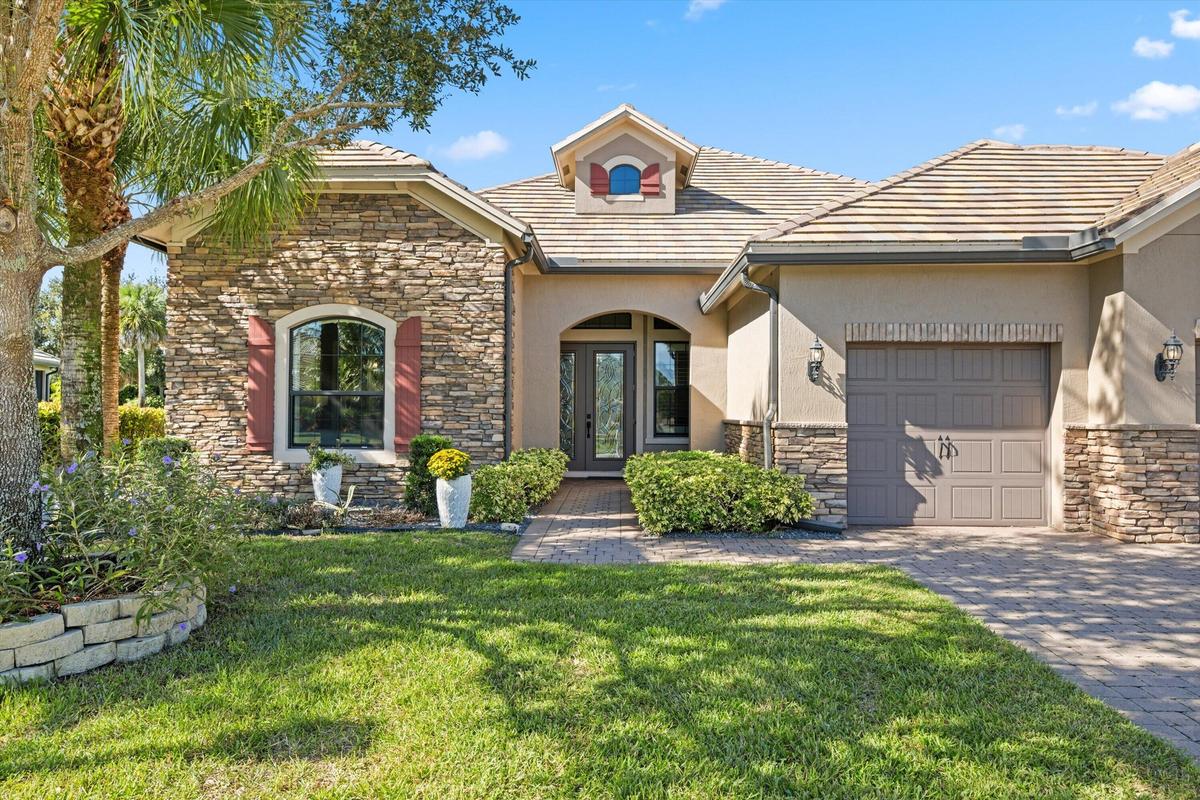 Single-story residence featuring a stone veneer and stucco facade, arched entryway, decorative shutters, and a paver driveway