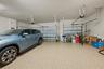 Three-car garage featuring epoxy-coated flooring, two individual metal roll-up doors, and ceiling-mounted automatic door openers
