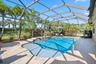 Screened-in patio featuring a paver deck, built-in swimming pool with step entry, stone-finished spillover, and surrounding palm trees