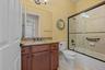 Bathroom featuring a vanity with stone-finish countertop, undermount sink, dark wood cabinetry, and a tub-shower combination enclosed by a framed glas