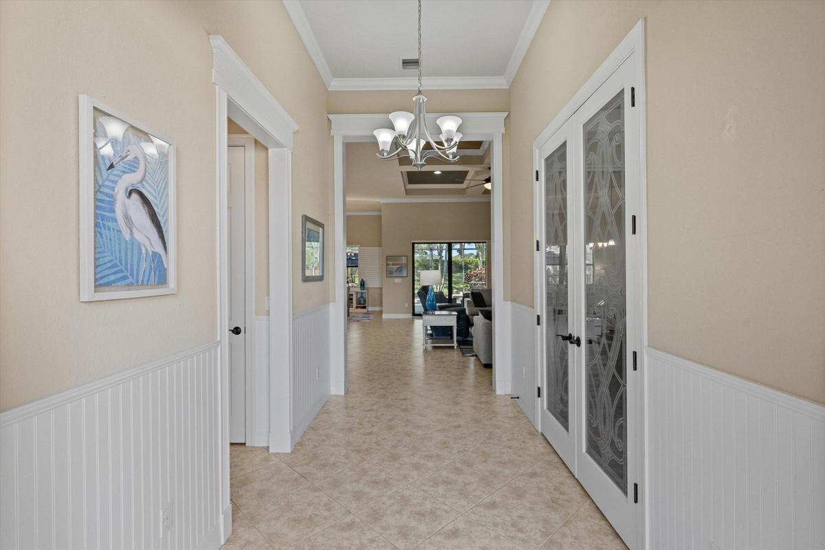 Foyer featuring white beadboard wainscoting, crown molding, tile flooring, a multi-arm chandelier, and glass-paneled French doors with decorative etch