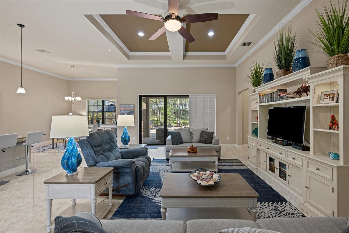 Coffered ceiling with recessed lighting, central ceiling fan, built-in floor-to-ceiling media cabinetry, tile flooring, and sliding glass doors