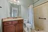 Bathroom featuring wood-finish cabinetry, stone-texture countertop, integrated sink, and walk-in shower with tile surround