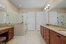 Bathroom featuring dual-sink vanity with stone-finish countertops, glass-enclosed shower, dedicated vanity seating area, and tile flooring
