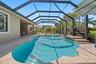 Screened-in patio featuring a custom-shaped pool, raised spillover spa, stone-finish decking, and exterior house access