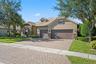 Stucco exterior featuring stone veneer accents, multi-gabled roofline, arched window detailing, three-car garage, and paved driveway
