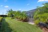 Screened-in patio enclosure featuring paver accent landing, surrounded by mature palms, manicured lawn, and professional landscape shrubbery